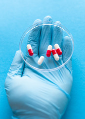 hand in a medical glove holds a petri dish with pills