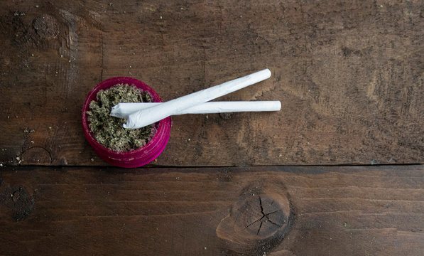 Political and world view debate question around alcohol and cannabis marijuana use. Ground up bud in a blue glass pipe and a bright pink grinder 