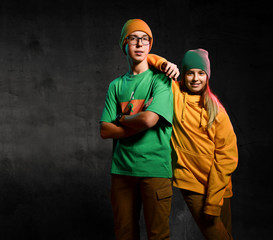 Young happy teens boy and girl in green and yellow stylish casual clothing and hats standing and...