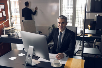 Mature attractive boss in suit working at computer indoors