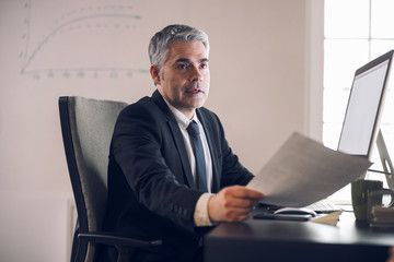 Mature boss keeping documents in hand indoors