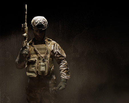 Soldier in desert uniform standing armed front view on dark background.