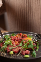 Young woman is eating beef tartare with egg yolk, using knife and fork, mixing up the meal