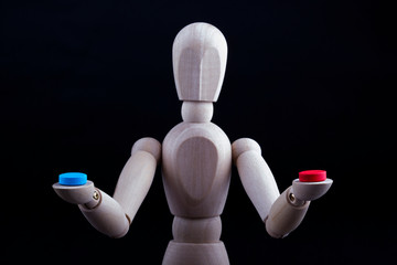 A wooden Gestalta doll or mannequin holds red and blue pills in its hands on a black background. The concept of choice.