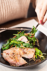 Close up of cutting fish fillet with lettuce with knife and fork