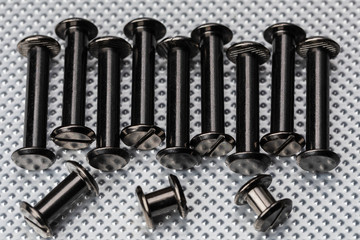 A Macro image of various sized Chicago Screws or Barrel Bolts of varying lengths on a stainless steel industrial background.