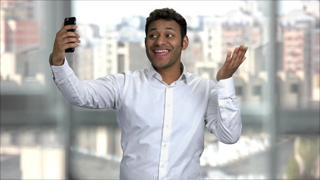 Young indian man posing and taking selfies. Selfie photo concept. Office worker shows different positive emotions, cityscape background.