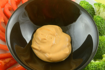 Creamy dip in black bowl with fresh raw red pepper slices and broccoli florets on plate