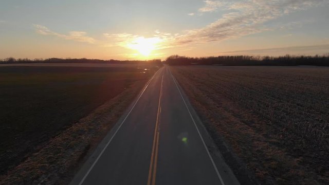 Rural road with farm fields flying into the sunset. Aerial, Empty road
