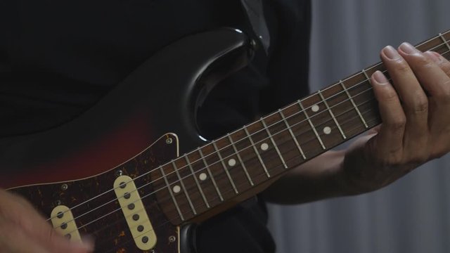 A man in black is playing a chord on an electric guitar at home, a sunburst guitar with rosewood neck.