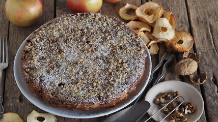 Round homemade fruit tart on a wooden ancient table with ingredients for sprinkling.Apple and plum chips are used. Place for text.