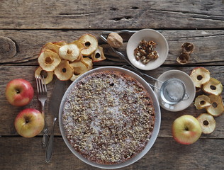 Round homemade fruit tart on a wooden ancient table with ingredients for sprinkling.Apple and plum chips are used. Place for text.