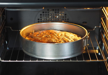 A round homemade fruit cake is baked in a kitchen oven.