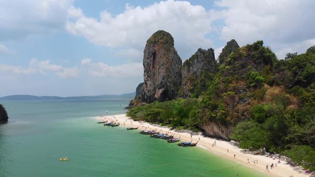 Blue ocean white sand tropical beach at railey phra nang beach thailand drone footage. Limestone cliffs rocks in the andaman sea torquiose vacation with long tail boats.