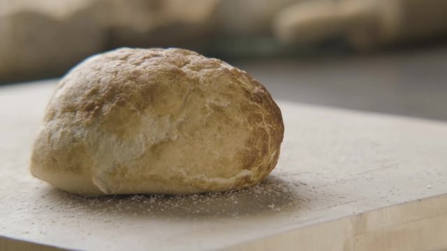 A fresh bakery style bun falls onto a wooden cutting board followed by a hand picking it up in slow motion.