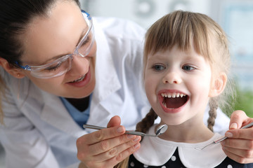 Woman dentist examines teeth in clinic at child. Doctor will monitor home dental hygiene. Dentist...