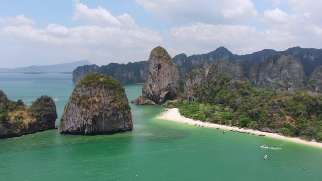 Blue ocean white sand tropical beach at railey phra nang beach thailand drone footage. Limestone cliffs rocks in the andaman sea torquiose vacation with long tail boats.
