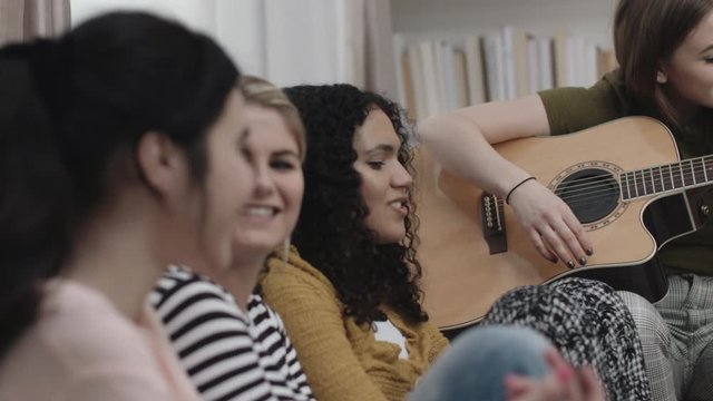 Group of female friends play guitar in student room