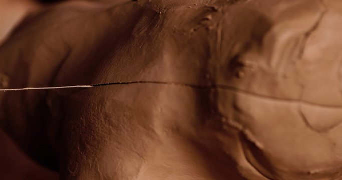 Young handsome sculptor cuts a piece of raw clay with a string. Artisan potter prepares material for his pottery. Strong male hands squeeze wet clay for modeling and sculpting. Work close-up.