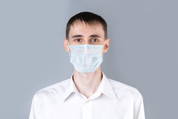 Man in a medical mask. A handsome dark-haired man in a white medical uniform, shirt and medical mask  looking at camera on a gray background. Chinese Coronavirus , Covid-19