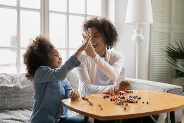 Sitting on sofa happy African little daughter gives high five to mother, family spend time together...