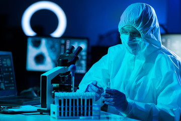 Scientist in protection suit and masks working in research lab using laboratory equipment:...
