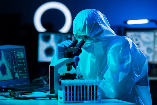 Scientist In Protection Suits And Masks Working In Research Lab Using Laboratory Equipment: Microscopes, Test Tubes. Coronavirus Covid-19 Hazard, Pharmaceutical Discovery, Bacteriology And Virology.