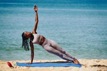 Strong woman doing side plank, outstretching arm and looking at fingers