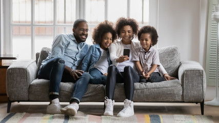 Horizontal image happy African ethnicity young family with small children having fun using...