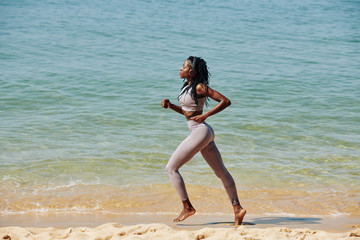 Fit slim young woman enjoying music in her headphones when jogging on the beach