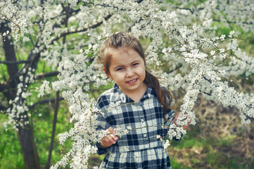 Portrait of a beautiful little girl at the flowering plants . Baby and cherry blossom . Spring walks in the fresh air
