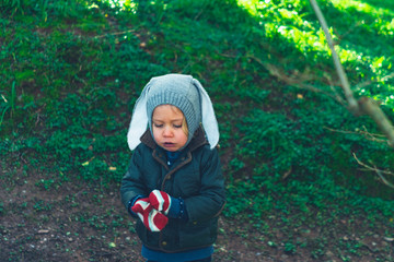 Little preschooler putting on his gloves in the woods