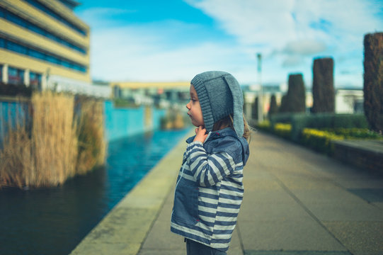 Little preschooler standing by artificial pond in the city