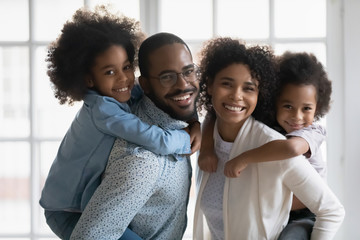 Portrait of African ethnicity parents piggy back son and daughter posing indoors. Pretty family...