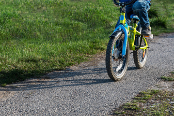 Fototapeta na wymiar A child rides a bicycle along the path, among the green grass in the sun. Close-up on wheels and pedal. The concept of balance on the road with copy space.