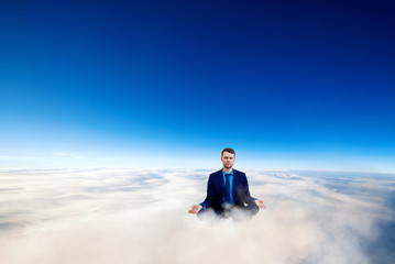 Fototapeta na wymiar Businessman sitting in lotus pose on white clouds in the sky.