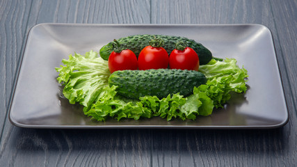 Fresh cucumbers and tomatoes and lettuce on a gray plate. vitamins and light breakfast