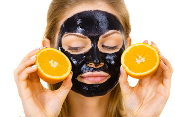 Girl black carbo mask on face holds orange fruit