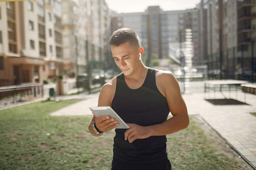 Man with a tablet. Guy in a sports clothes. Male in a summer park