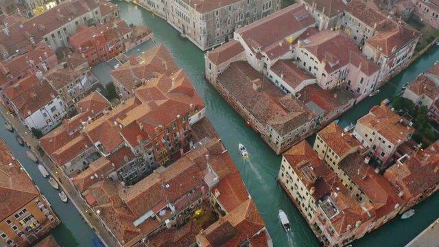 Aerial, drone shot following boats on a channel, during sunset, in Venice city, Italy