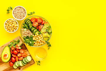 Healthy salad bowl with quinoa, avocado and chickpeas on yellow background top-down copy space