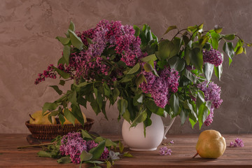 Spring still life lilac with a white vase with fresh pears on a wooden table against the background of an old wall