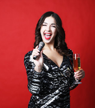 Young woman in black evening dress holding glass of champagne and microphone.