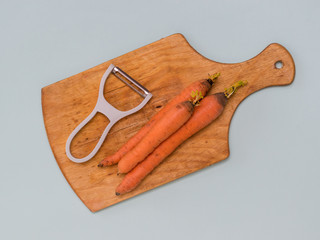 Three carrots and a peeler on a cutting Board on a blue background.