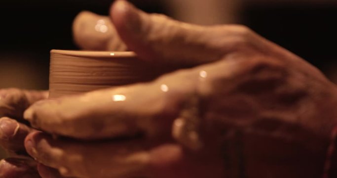 Young handsome sculptor shapes the clay product with pottery tools. Artisan potter prepares material for his pottery. Strong man hands working clay on potter's wheel. Work close-up.