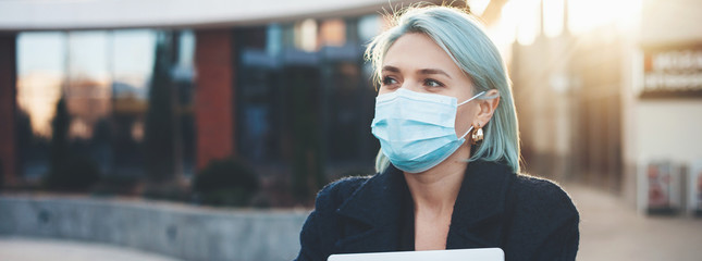 Blue haired caucasian woman posing outside with a computer while wearing a special mask