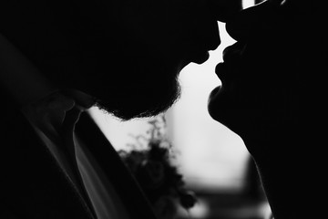 Close-up of the silhouette of a bride and groom a moment before the kiss. Black and white photo in backlight.