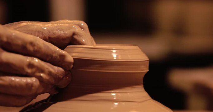 Young handsome sculptor shapes the clay product with pottery tools. Artisan potter prepares material for his pottery. Strong man hands working clay on potter's wheel. Work close-up.