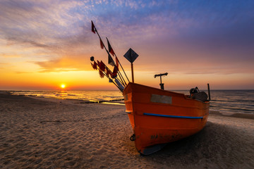 Colorful fishing boat on a sandy sea beach during a beautiful sunset