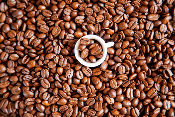 A small white cup of coffee stands on coffee beans.